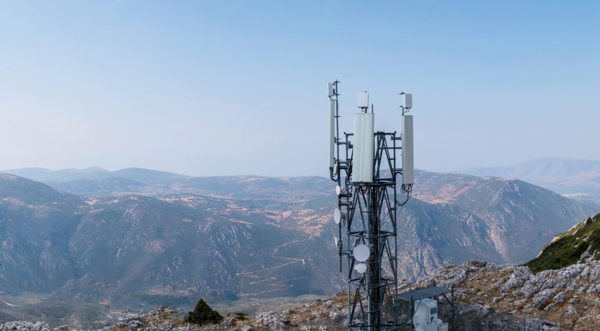 Cell phone tower. Cellular antenna, 5G radio network telecom transmitter aerial view. Rocky mountain and sky background