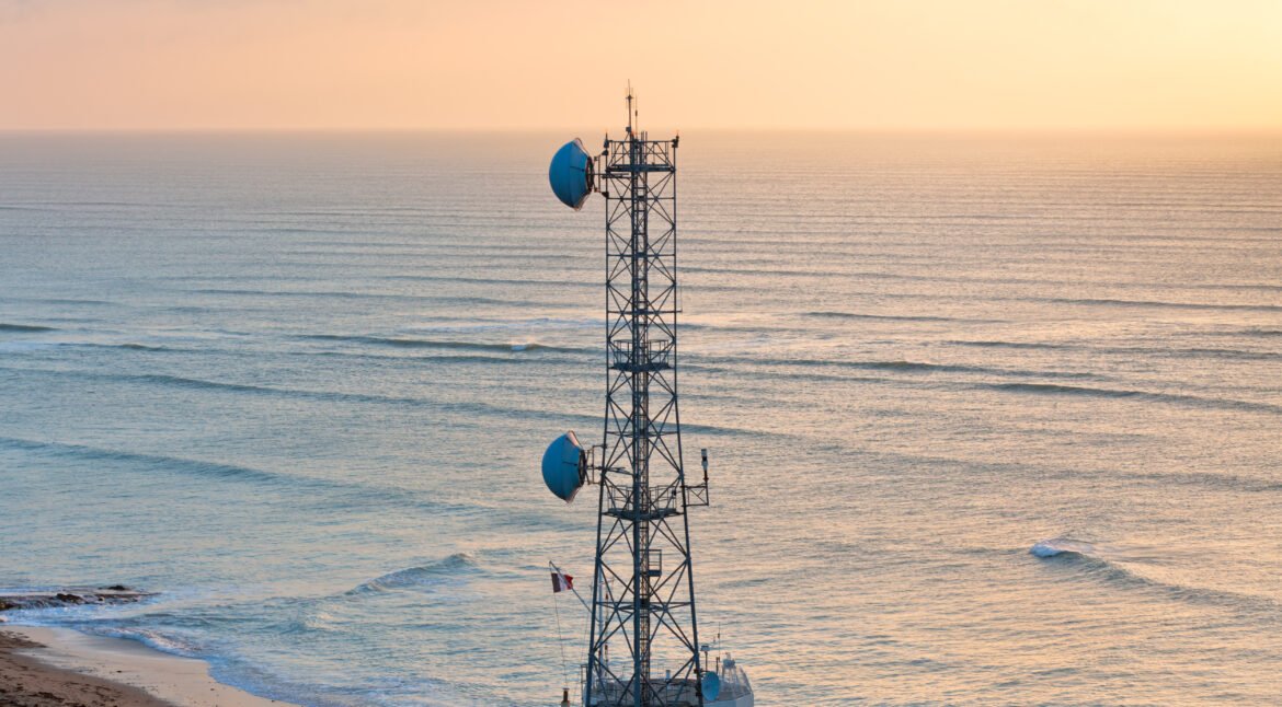 A radio communications tower with dishes against blue ocean and sky